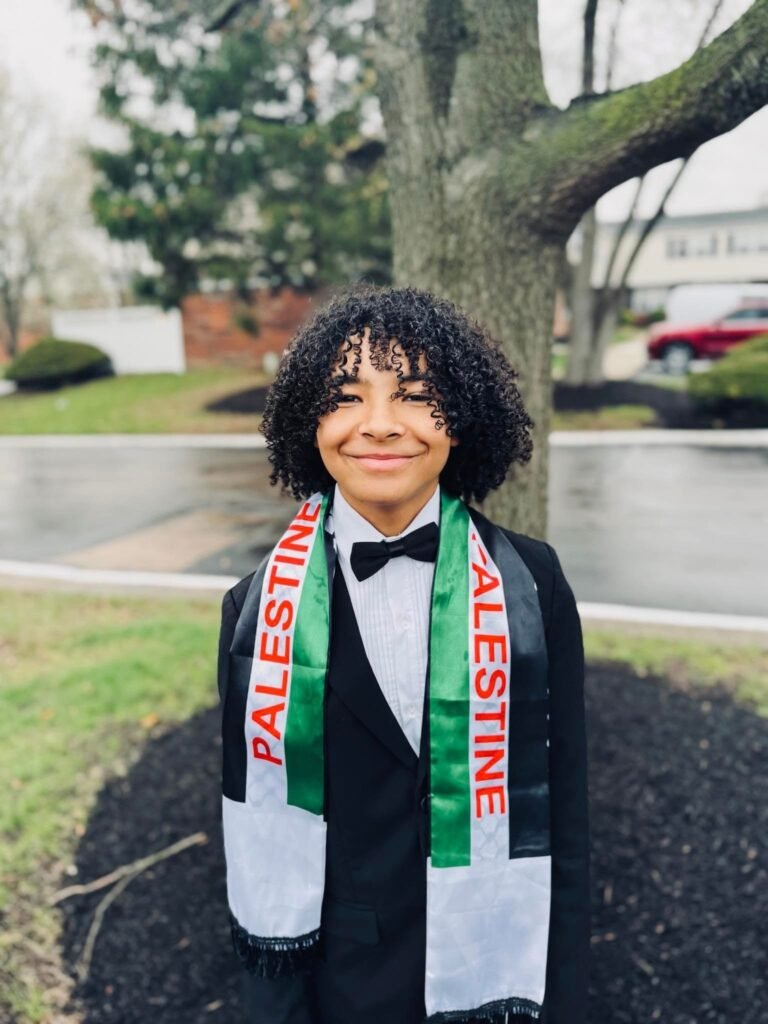 An Abule student smiling outdoors, wearing a scarf that reads Palestine